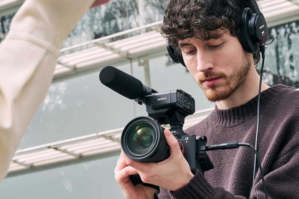 Immagine d'utilizzo con un uomo che indossa le cuffie connesso ad α7R VI con l'adattatore XLR XLR-A4 e il microfono shotgun ECM-778 montati, per registrare audio e video.